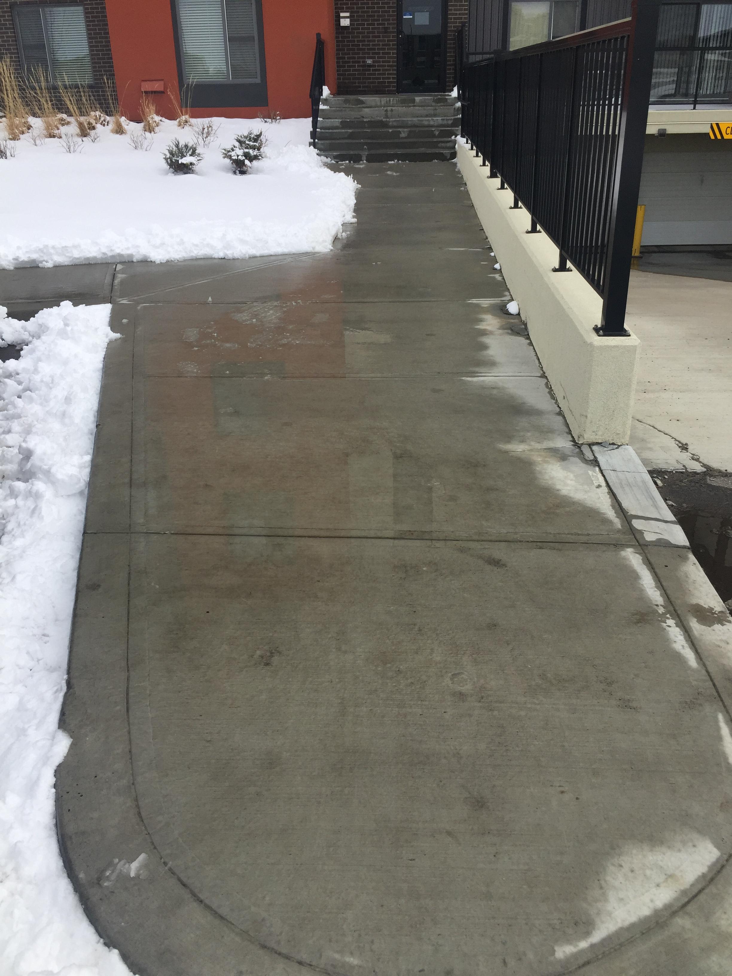 Commercial walkway cleared beside apartment building, snow piled to sides
